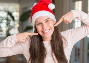Woman in holiday hat pointing to her smile