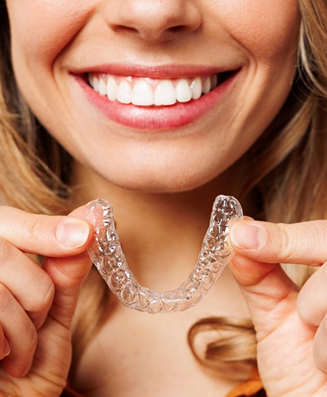 A woman holding clear aligners in front of her face