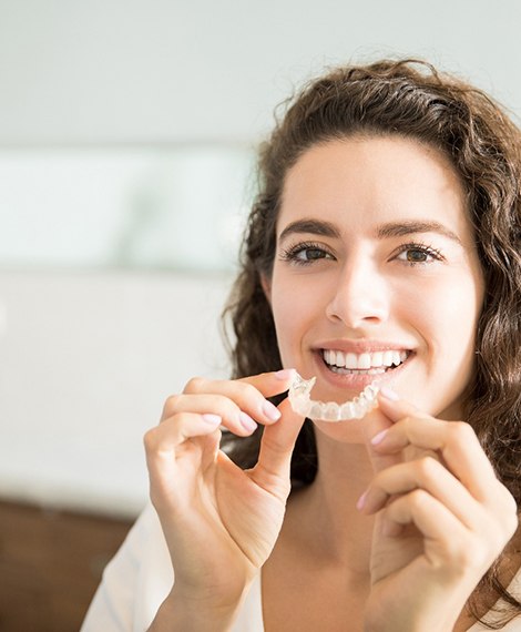 A smiling woman holding a clear aligner in a dental clinic