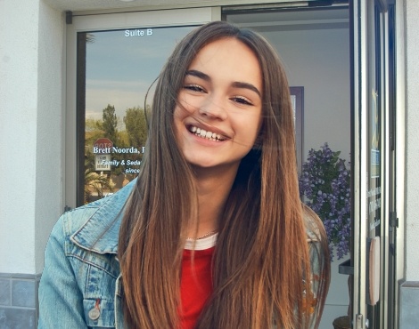 Young woman in denim jacket grinning outside of Henderson dental office