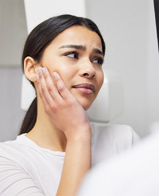 Woman in dental office holding her hand to her jaw looking at imaging