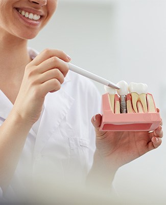 Nose-to-chest image of woman pointing to sample dental implant with pen