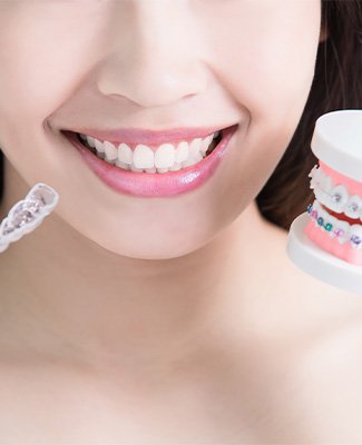 Nose-to-clavicle view of woman holding sample braces in one hand and a clear aligners tray in the other