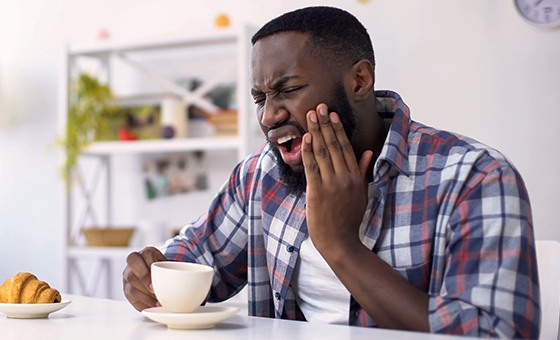 Man sitting at table holding his cheek in pain