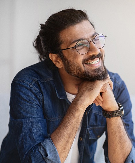 Man in denim shirt and glasses with braces smiling