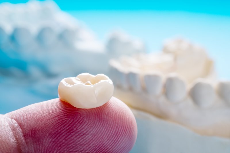 an up-close view of a dental crown resting on the tip of a person’s finger