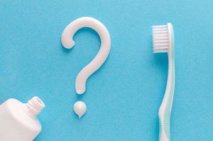 A question mark formed from toothpaste next to a toothbrush on a blue background